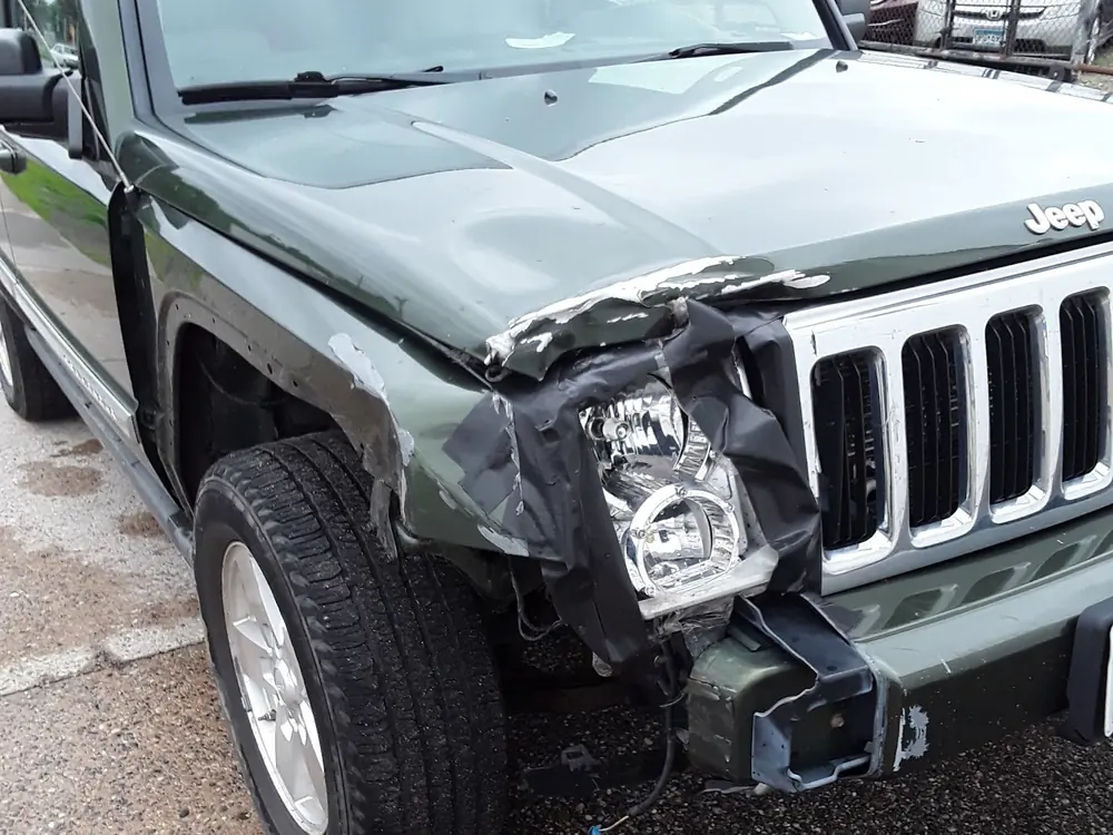 A green SUV front end with a broken headlight and grille, and a cracked, pushed-in bumper.