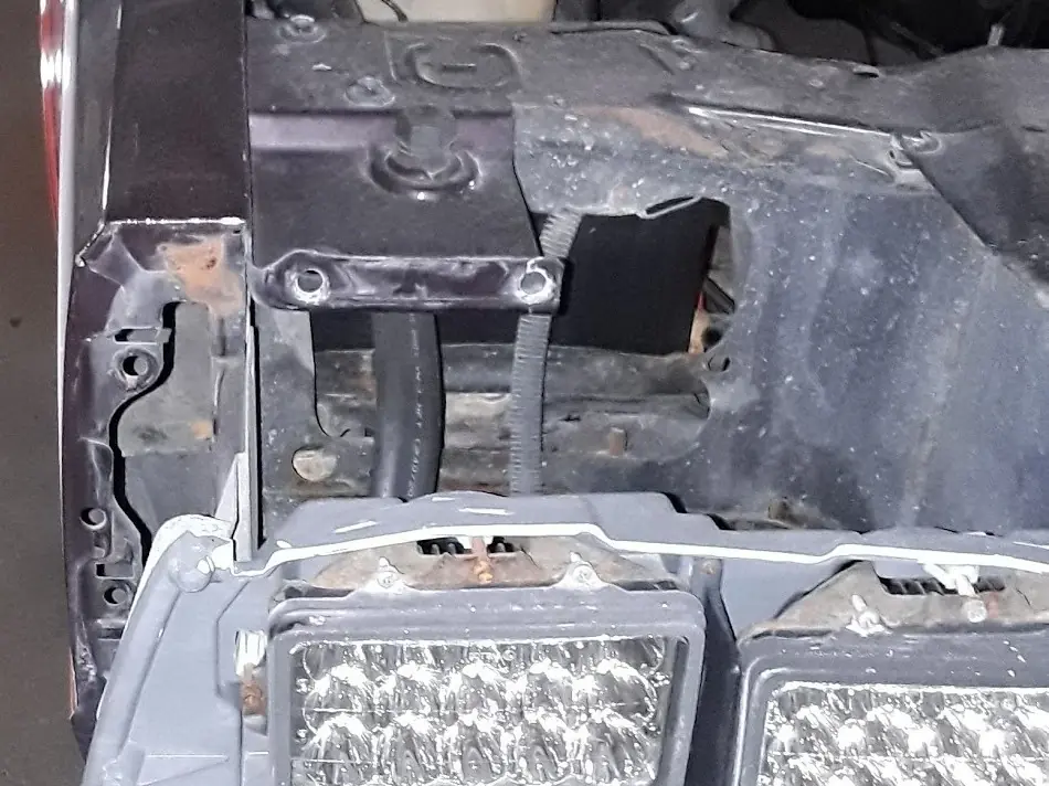 A car in the shop with the front bumper cover removed, exposing the support structure and lamps behind it.