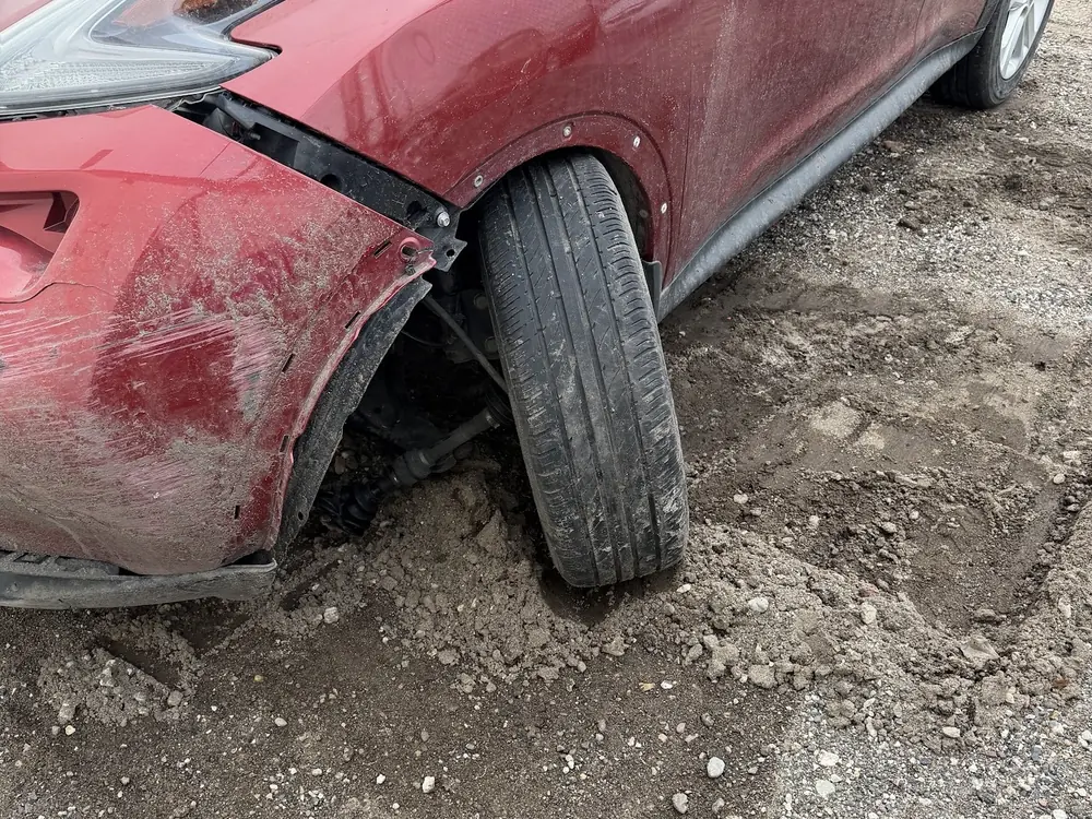 A red crossover whose front wheel is pushed back behind a torn bumper, a sign of possible damage behind the bumper and in the suspension that cannot be judged from outside.